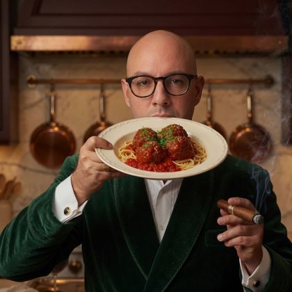 Dan DeCristoforo in a green velvet smoking jacket, holding a plate of meatballs and a lit cigar